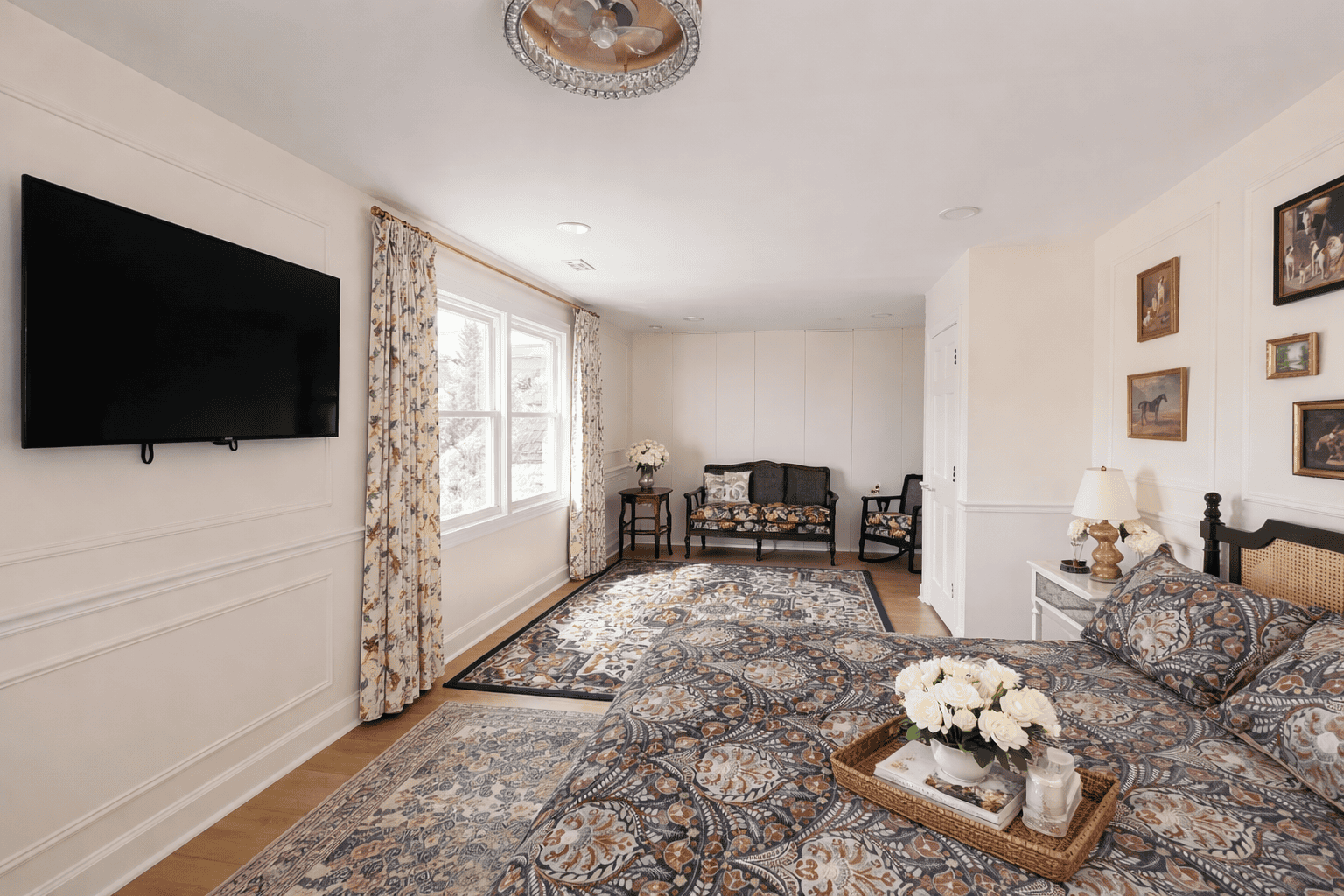 bedroom in Laurel Haven Estate’s Dogwood Suite featuring a king bed with patterned bedding, added decorative tray with flowers, soft patterned curtains, wall-mounted TV, and a cozy seating area with elegant furnishings and natural light.