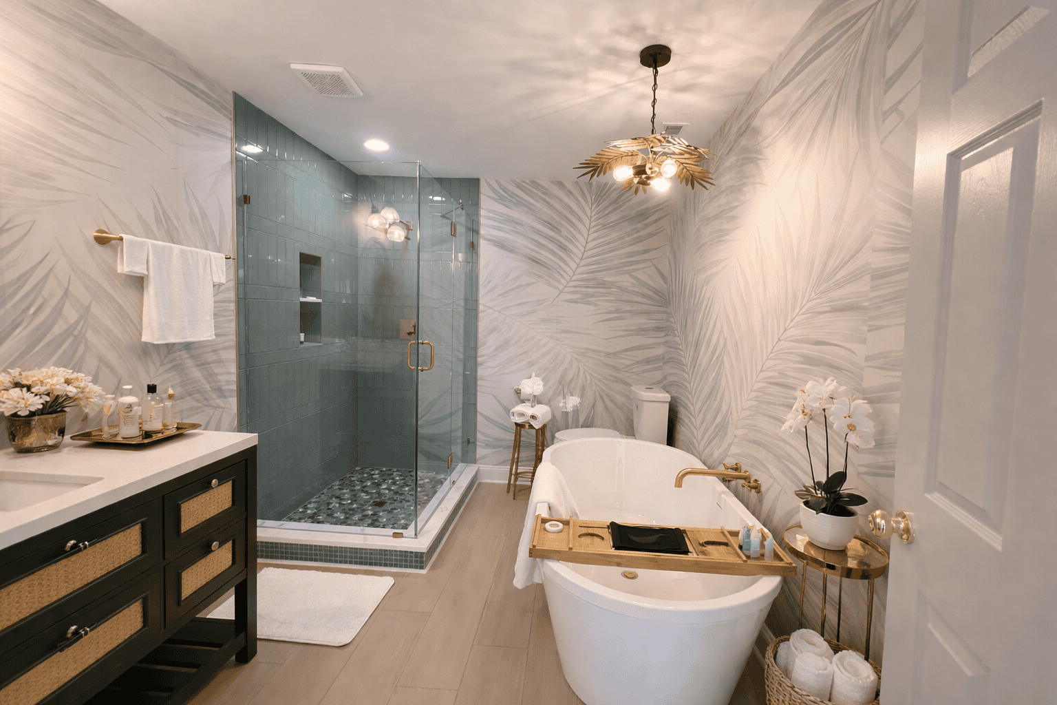 Elegant, spa-style bathroom in Laurel Haven Estate’s Dogwood Suite featuring a freestanding soaking tub with bath tray, glass-enclosed walk-in shower, tropical leaf wallpaper, and styled accessories including fresh flowers, folded towels, and gold accent décor.