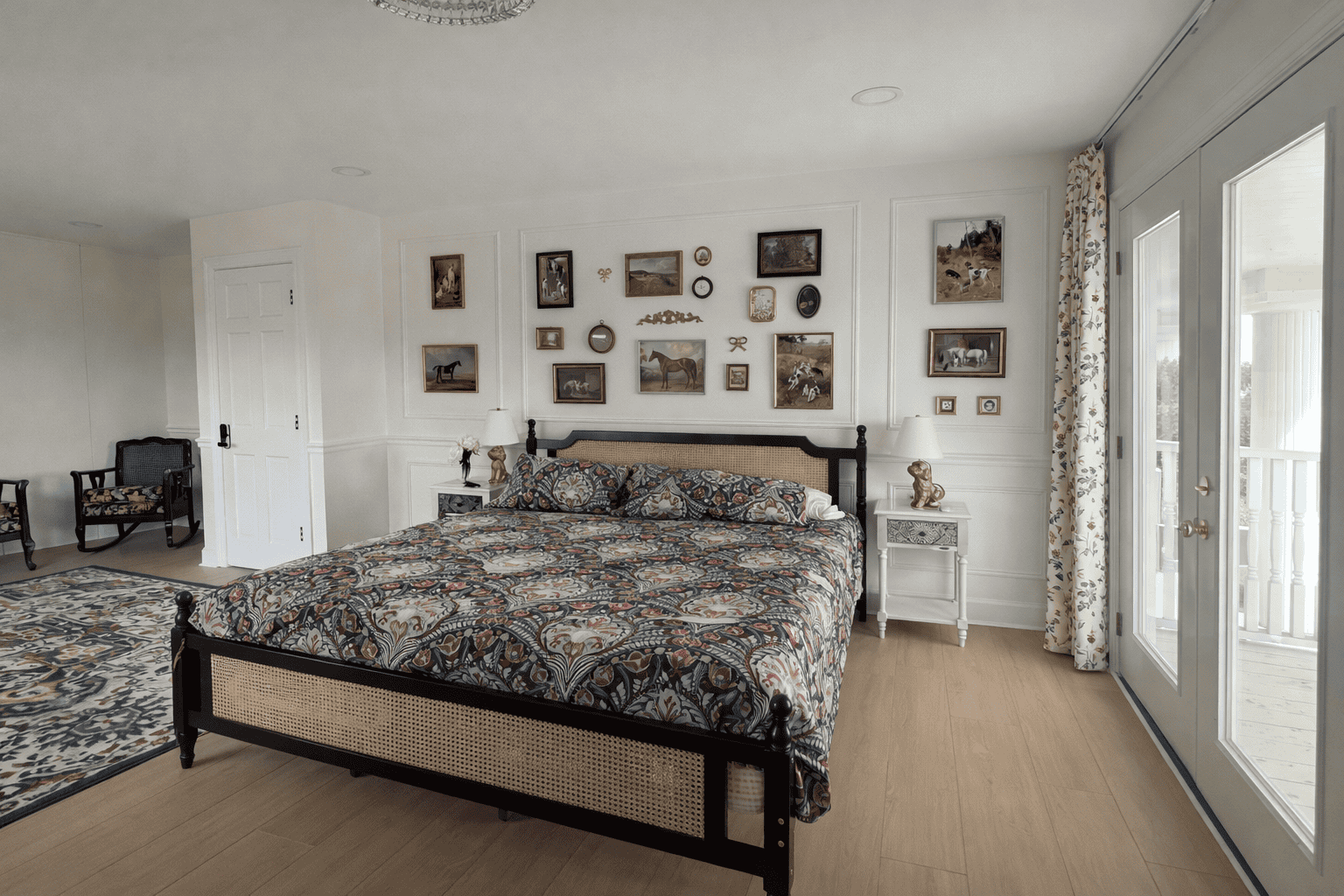 Charming, spacious bedroom in Laurel Haven Estate’s Dogwood Suite featuring a king bed with patterned bedding, curated gallery wall above the headboard, elegant bedside tables with lamps and décor, and French doors with soft curtains leading to a private balcony with scenic views.