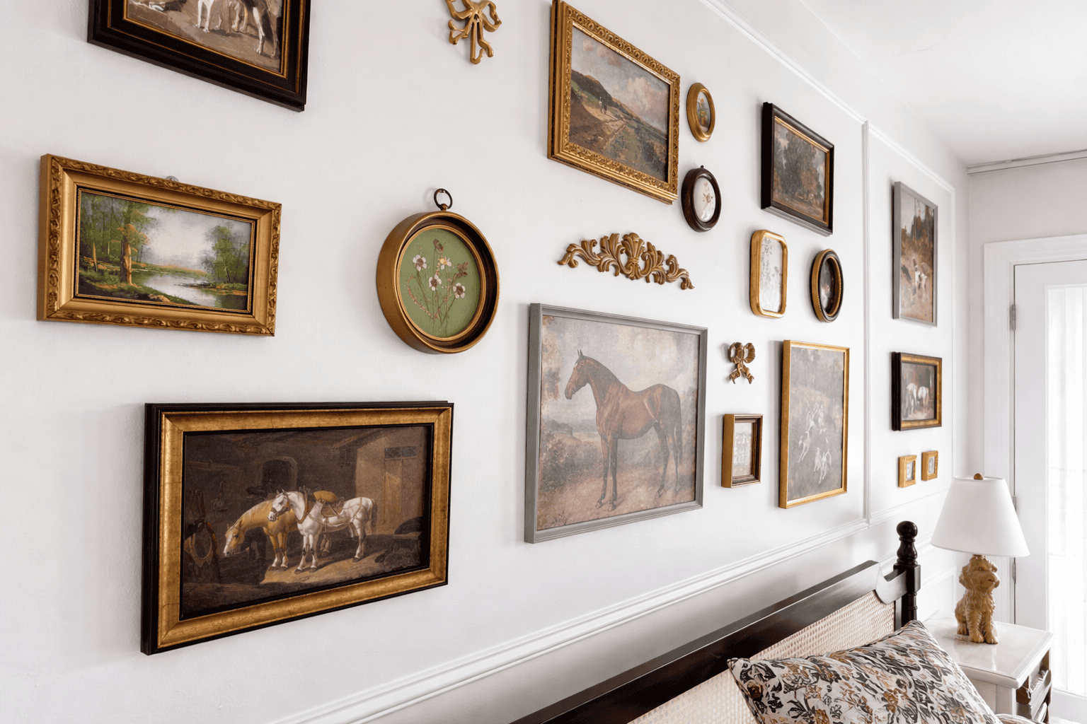 Elegant gallery wall in Laurel Haven Estate’s Dogwood Suite featuring a curated collection of vintage artwork in gold and wood frames above a classic bed, styled with soft lighting and refined décor for a real estate-ready look.