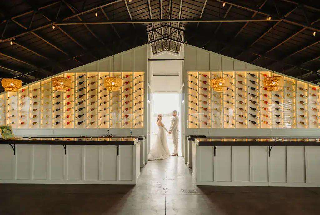 Wedding couple framed by glowing wine bottle walls and rustic lights.