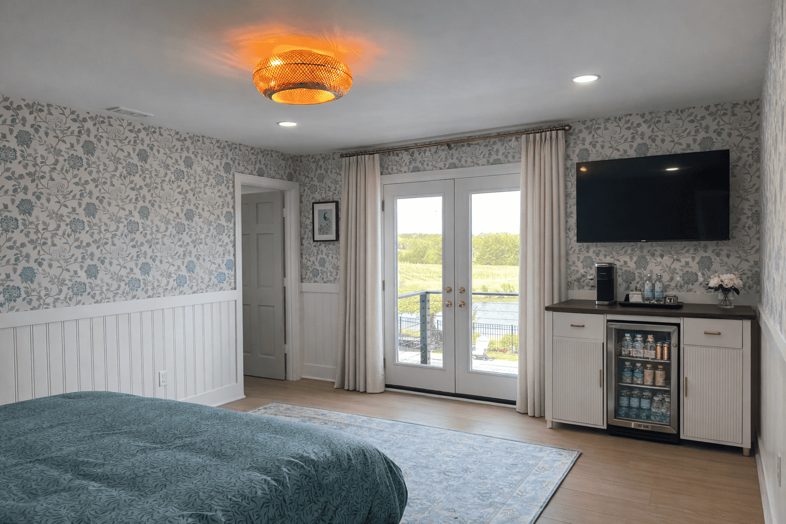 Jessamine Suite at Laurel Haven Estate in Lancaster SC featuring Romeo and Juliet balcony doors overlooking vineyard, pond, and pool, with elegant decor, curtains, and in-room bar with mini fridge