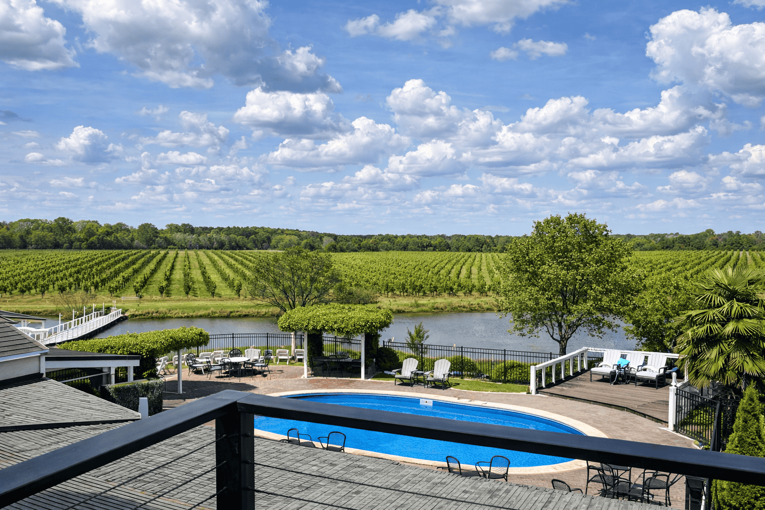 Scenic view at Laurel Haven Estate in Lancaster SC featuring vineyard rows across rolling fields, pond, pool, ceremony seating, and lush green trees under a bright sky